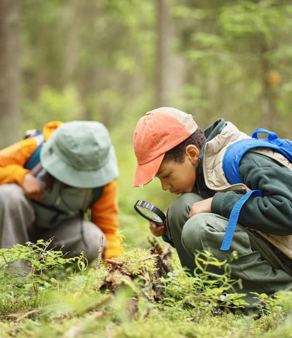 Due bambini esplorano il sottobosco con una lente d’ingrandimento
